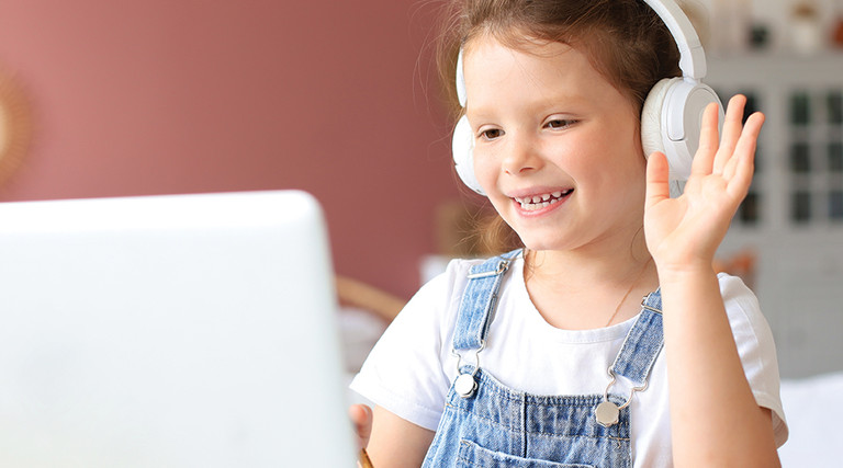 girl in headphones waving at computer screen 